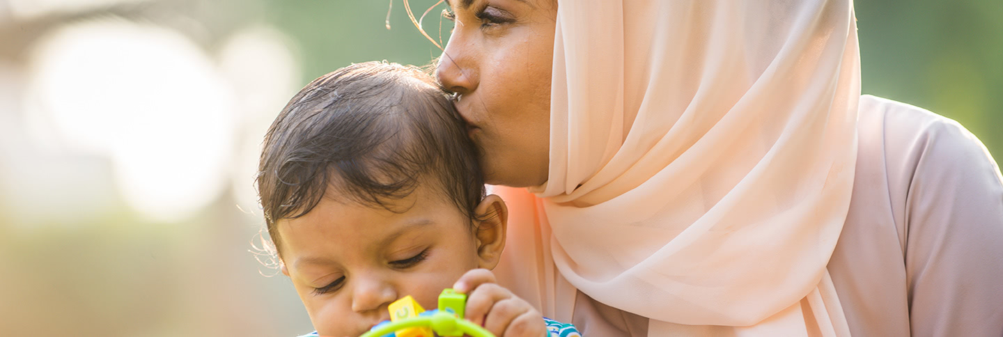 A Muslim woman kisses her child which he plays with a toy