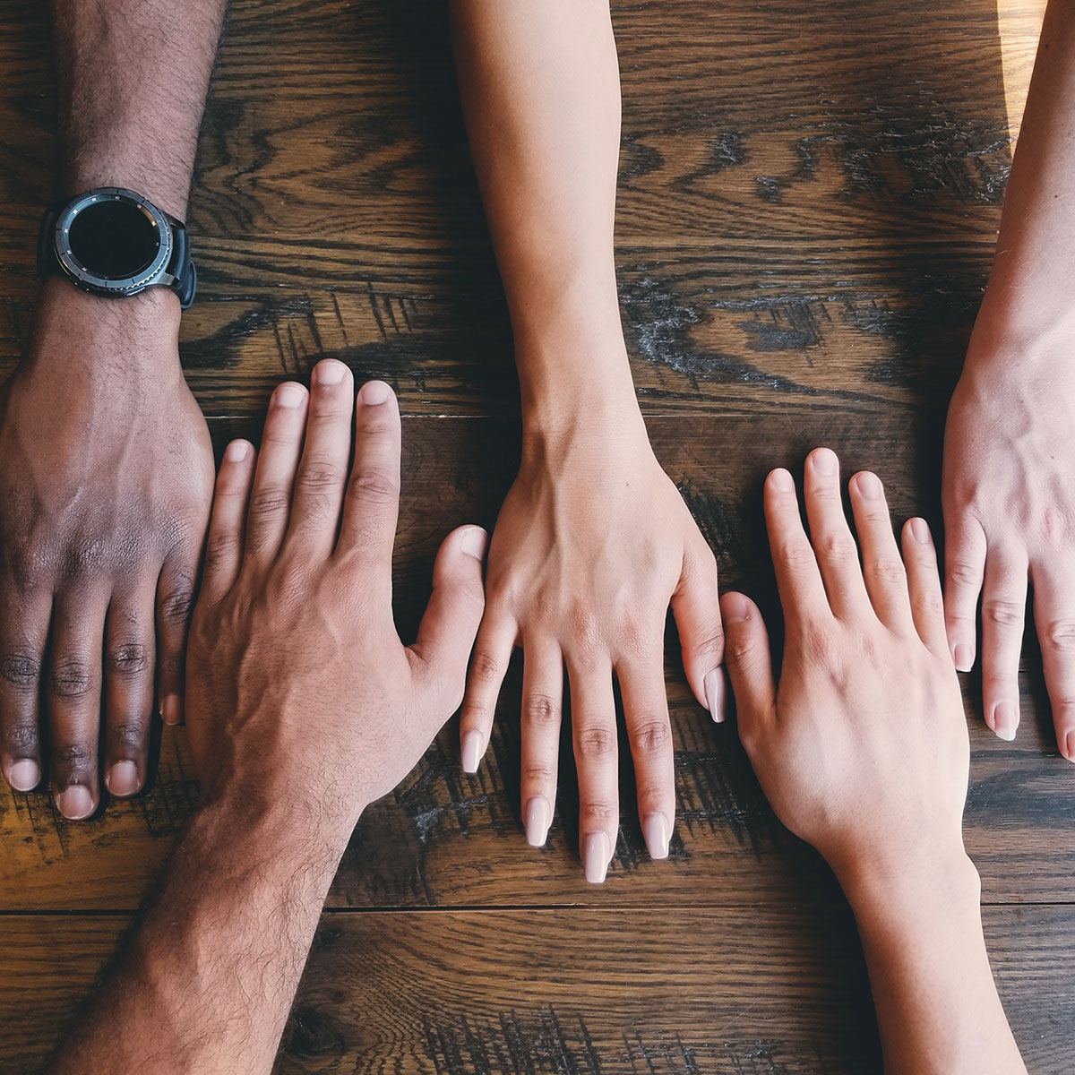 Diverse shades of skin tones are represented by hands placed flat on a desk