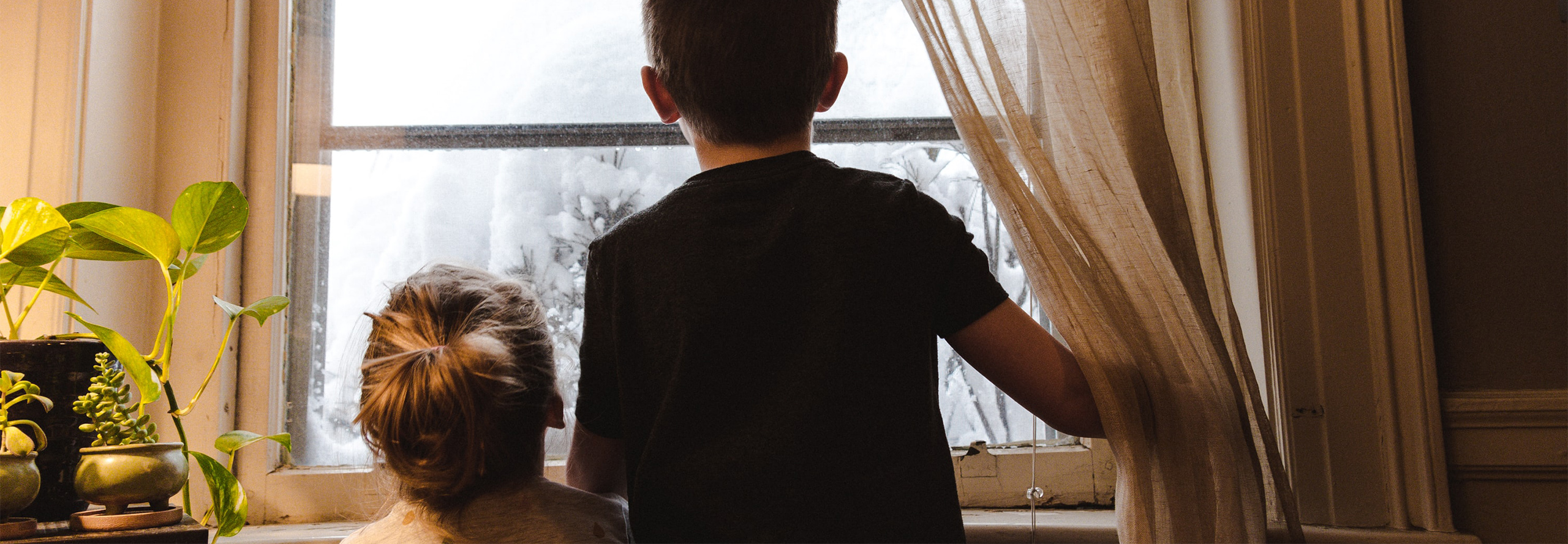 Two small children look out of their window at the snow falling.
